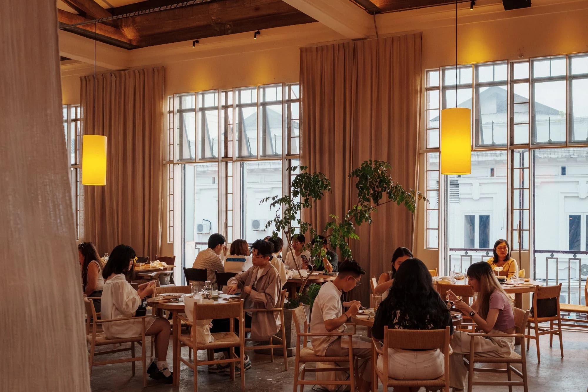Guests at tables in a warm restaurant with tall windows.