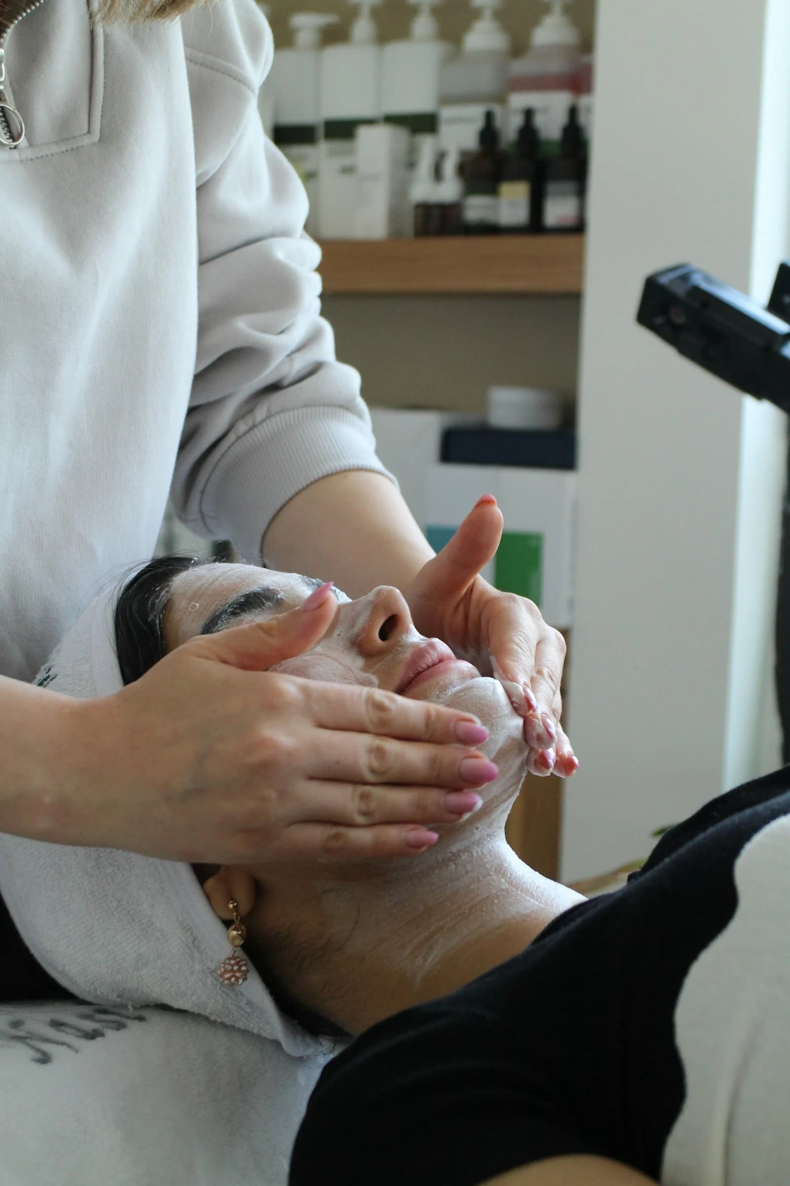 An esthetician's hands at work on a client's face in soft window light.