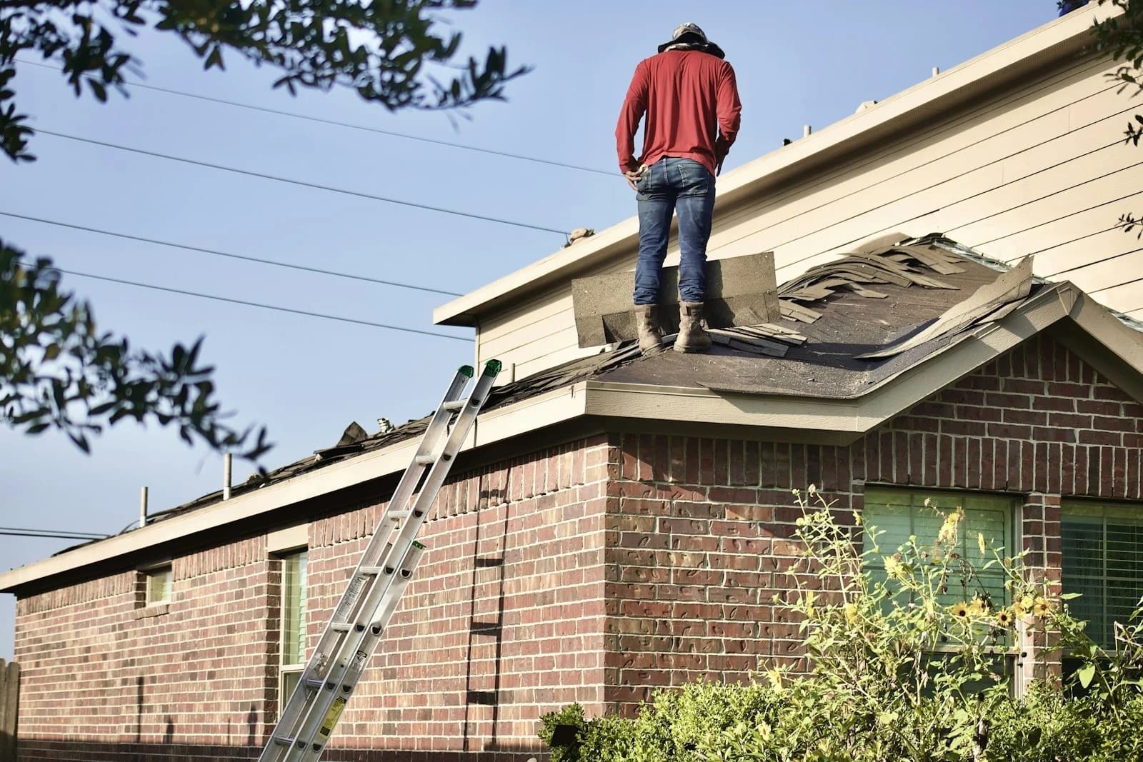 A roofer standing on a half-stripped roof of a brick house.